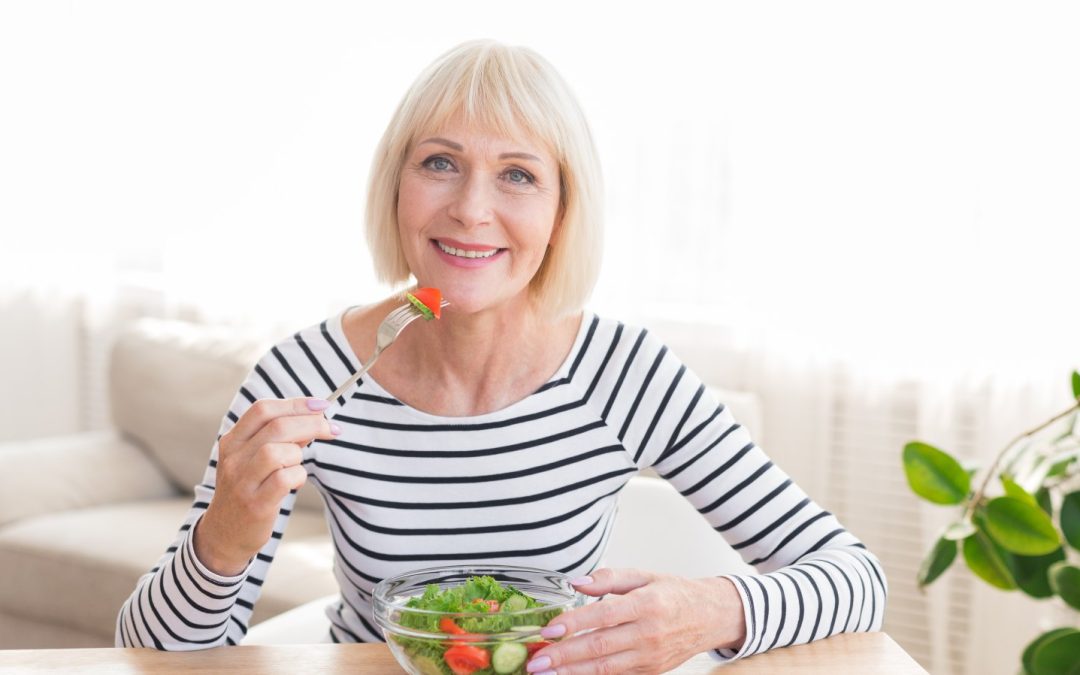 A happy senior woman eating a fresh, healthy salad at home