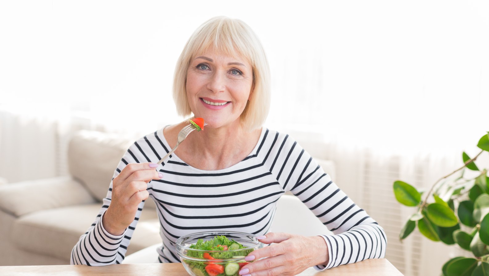 A happy senior woman eating a fresh, healthy salad at home
